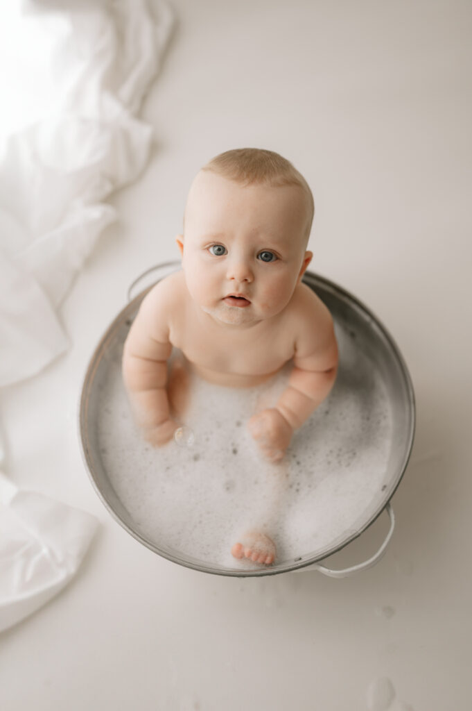 baby boy lying in the bubble bath in york photography studio smiling at the camera