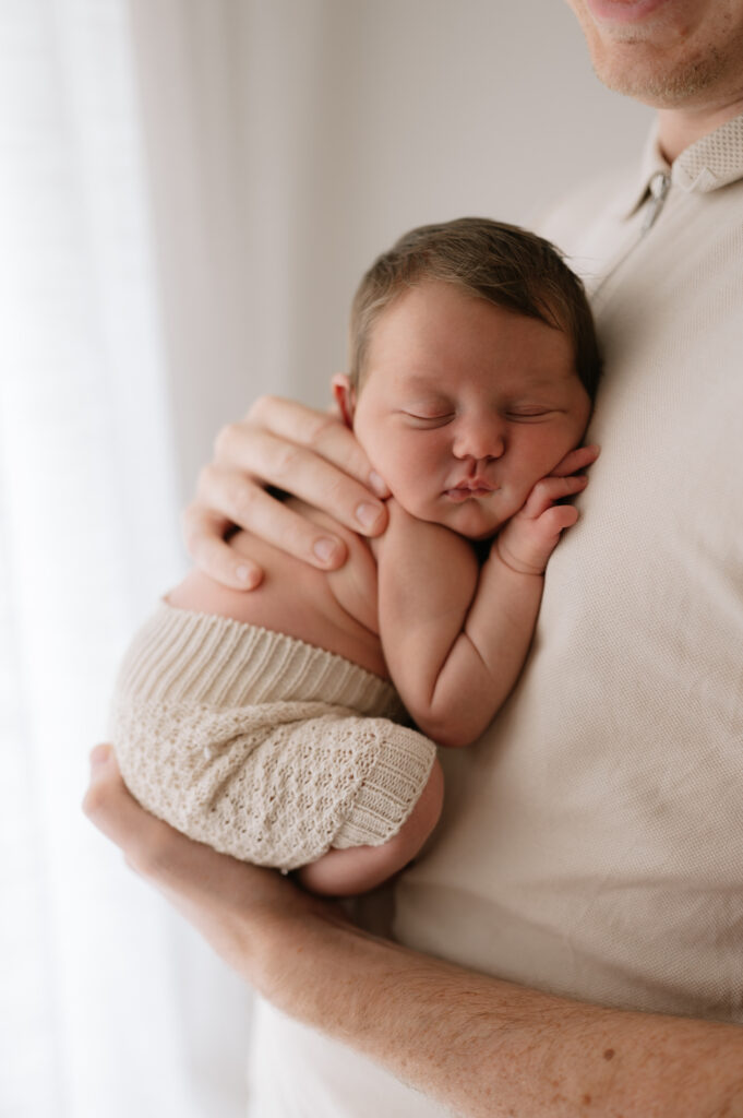 newborn baby girl on her dad curled up